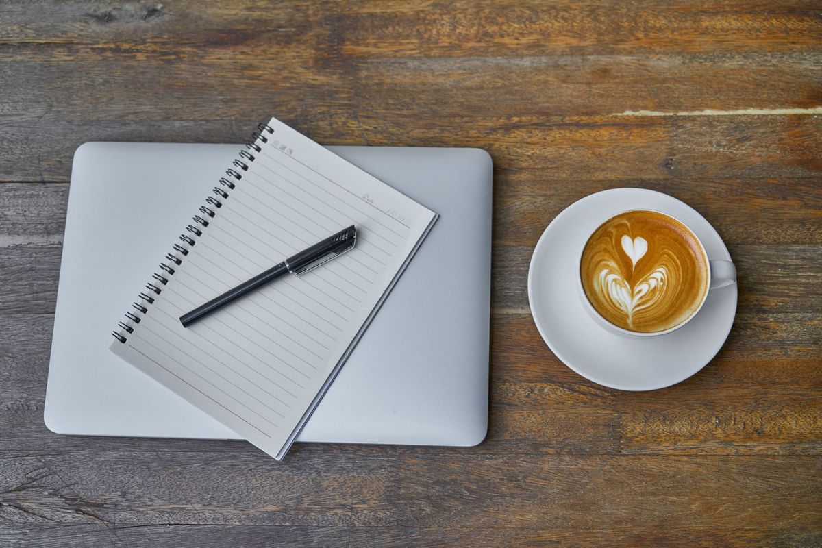 Mesa de trabalho com café, caderno e notebook